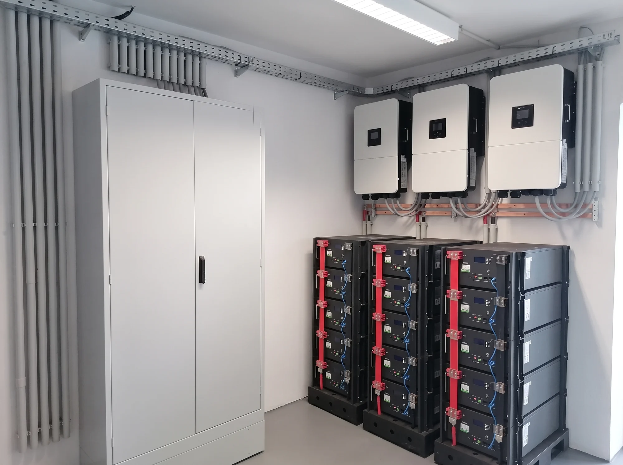 Utility room of a completed COR.stor installation: three battery racks with five packs each, three hybrid inverters mounted above them, control cabinet alongside