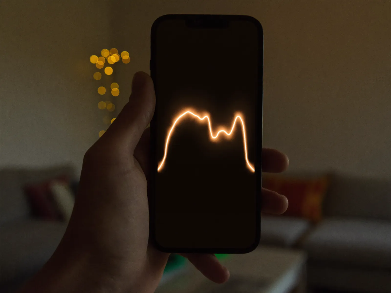 Hand holding a smartphone in a dark living room, a glowing curve on the display