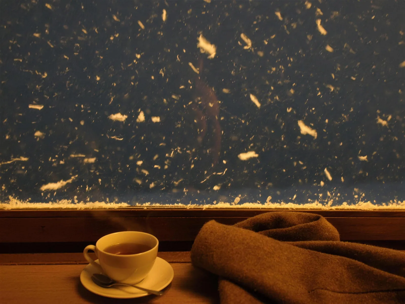 Schneetreiben vor dem Fenster, innen dampfender Tee und warme Decke
